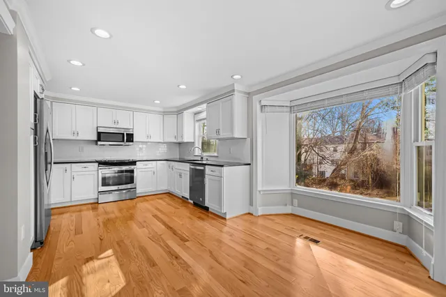 a kitchen with stainless steel appliances granite countertop a refrigerator oven a sink dishwasher and white cabinets with wooden floor