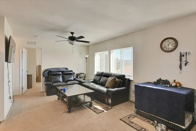a living room with furniture a clock on wall and a ceiling fan