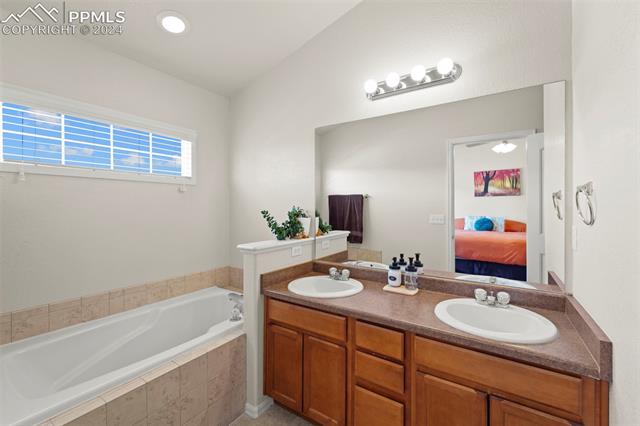 6310 Pilgrimage Road Colorado Springs, CO 80925 - Photo 23 of 31 Bathroom with tiled tub, vanity, and vaulted ceiling