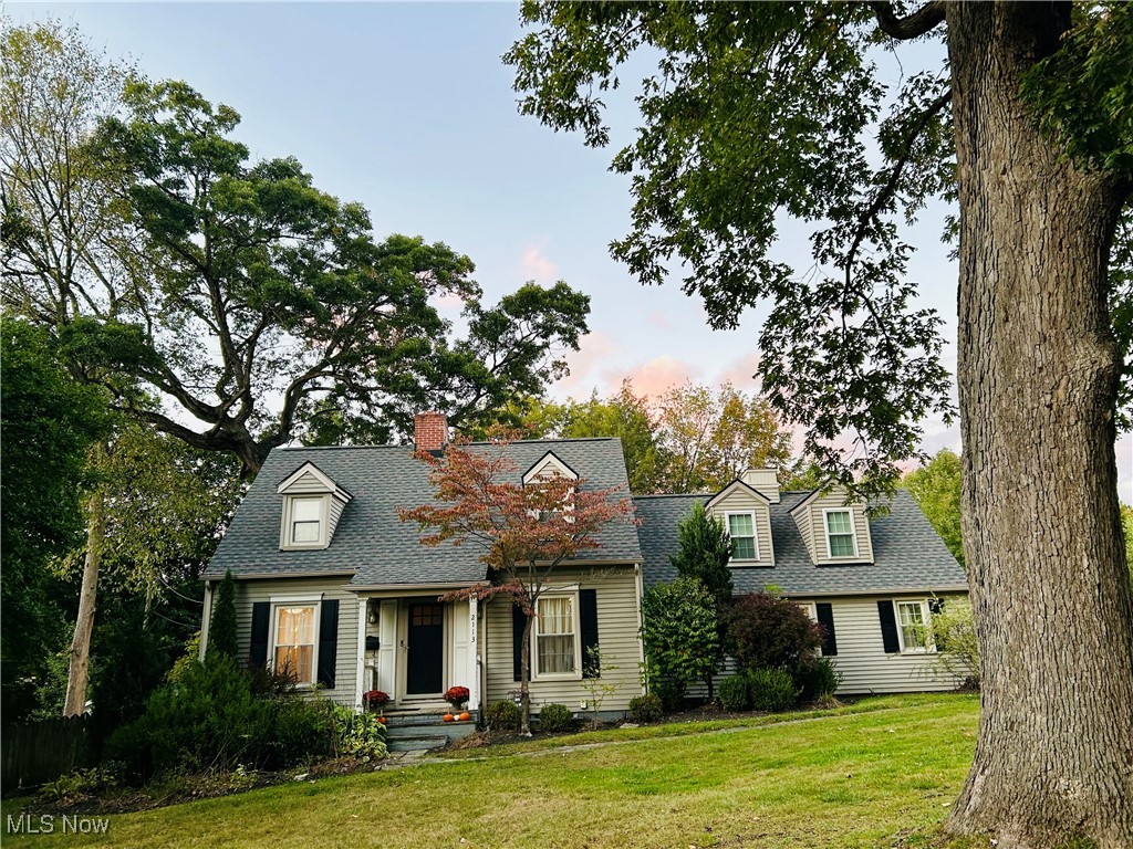 New england style home featuring a front yard, a chimney, and a shingled roof