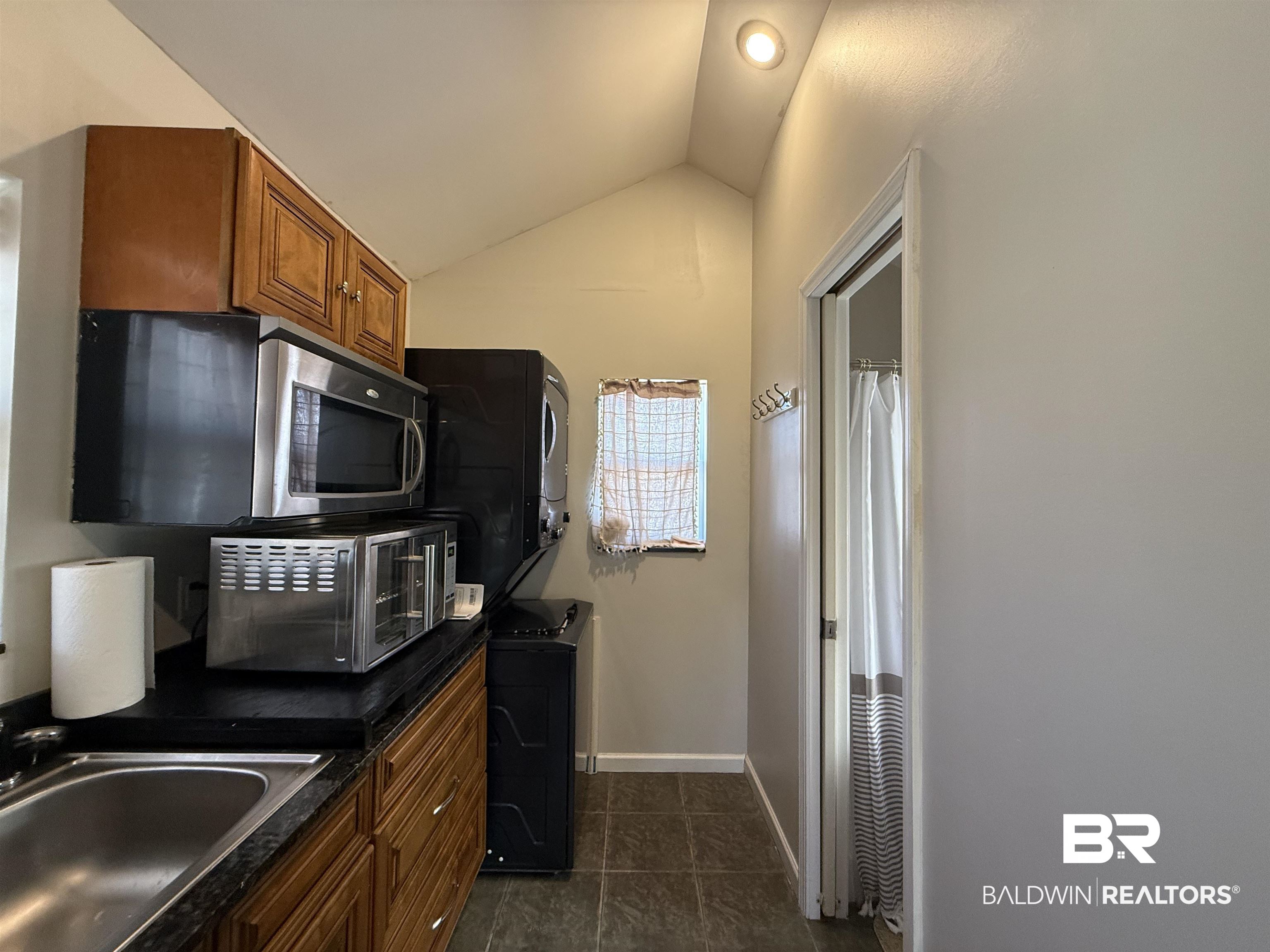 28114 Preserve Trail, Unit 190 Elberta, AL 36530 - Photo 30 of 69 Kitchen with wood finish cabinetry, vaulted ceiling, stacked washing machine and dryer, and dark tile patterned flooring