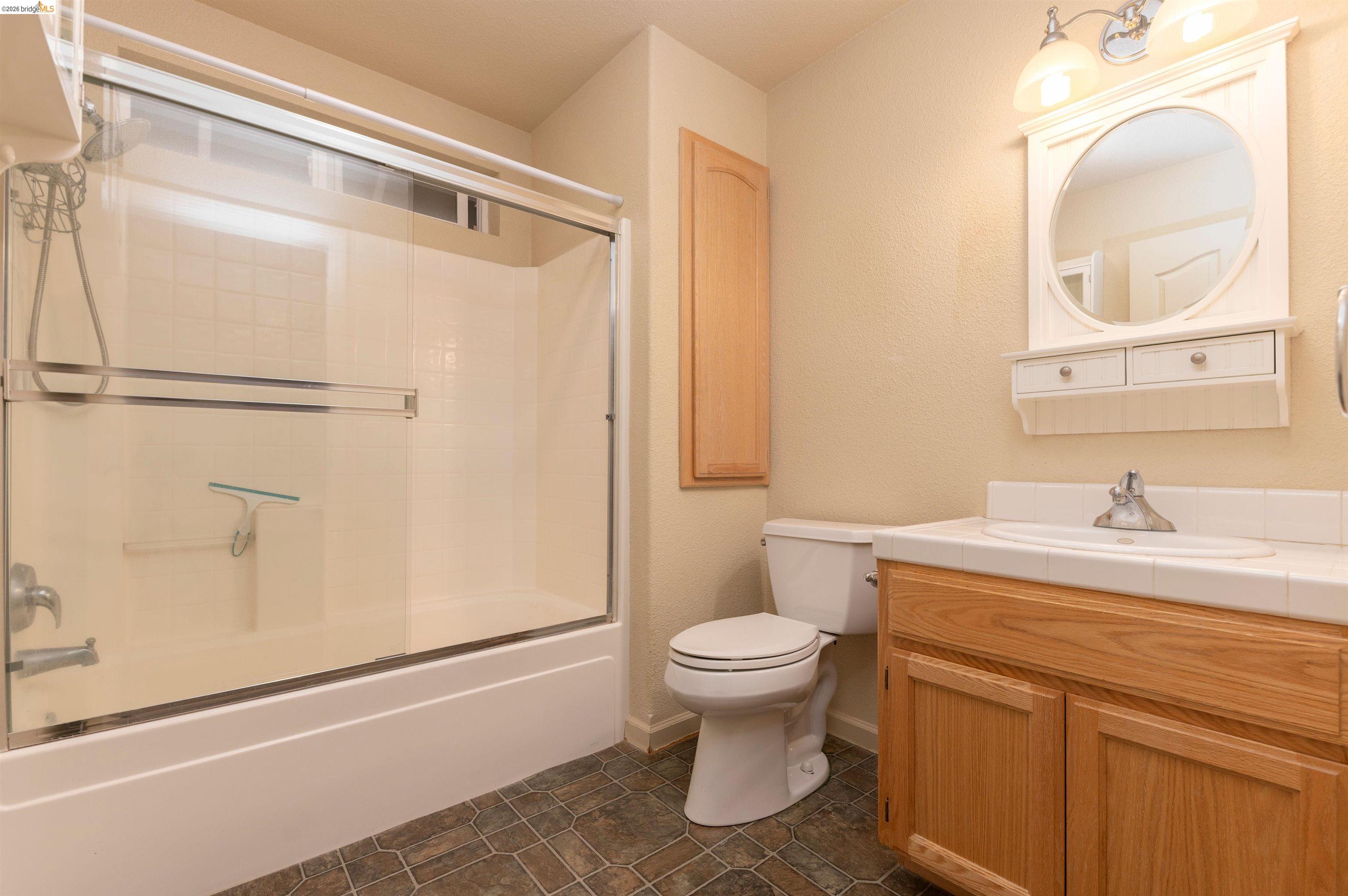 22401 Ridge Road Twain Harte, CA 95383 - Photo 29 of 56 Bathroom featuring a tub-shower combination with sliding glass doors, a vanity with a white countertop and natural wood-finish cabinetry, a toilet, and a wall-mounted medicine cabinet with an integrated shelf