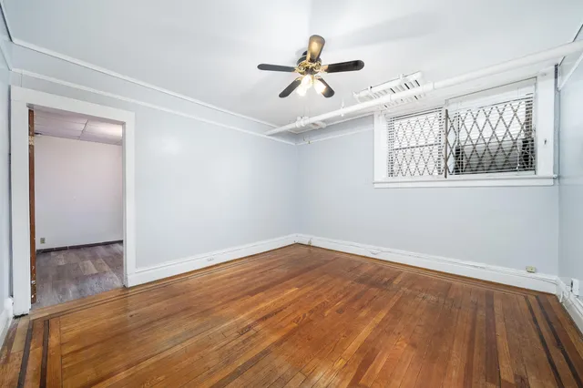 a view of an empty room with wooden floor and a ceiling fan