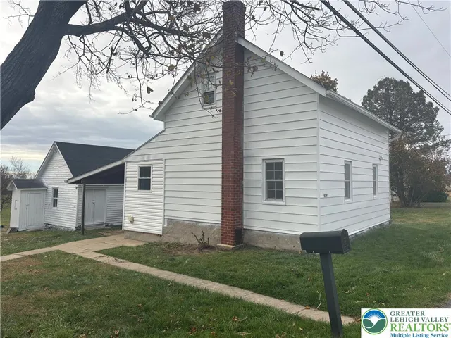 a view of a white house next to a yard with big trees