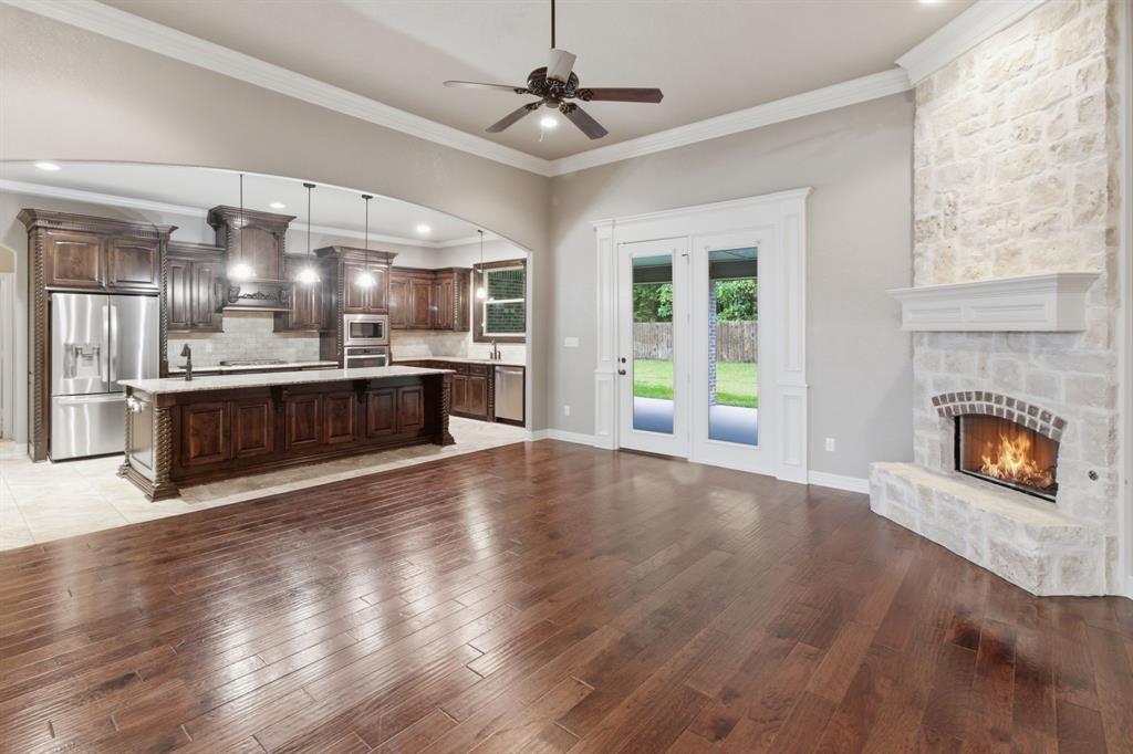 7765 Hickory Spring Lane Tyler, TX 75703 - Photo 16 of 38 Open-concept living area featuring rich wood-finish flooring, a stone-clad fireplace with a white mantel, and double glass-paneled doors opening to the exterior