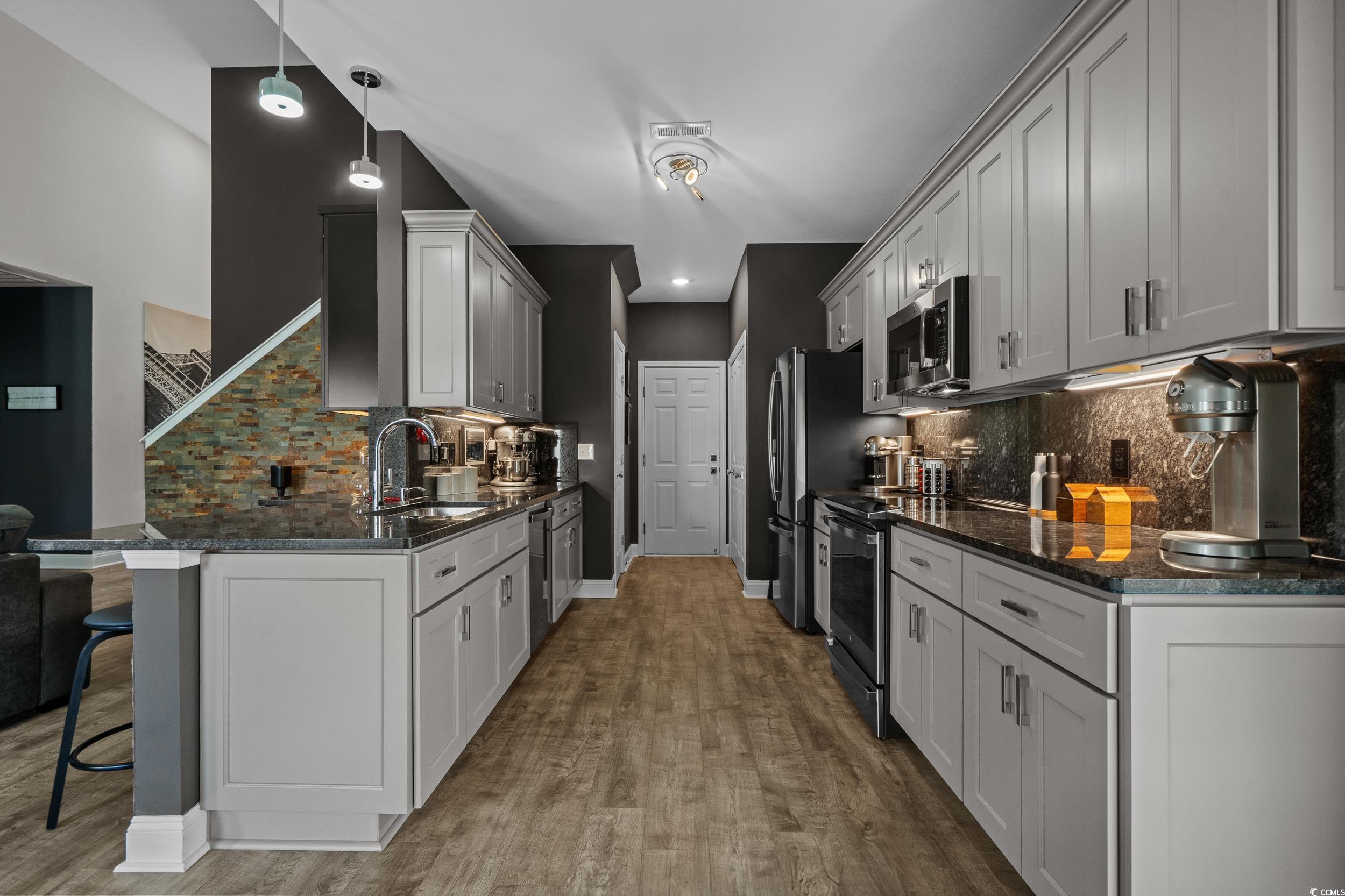 752 Hobonny Loop Longs, SC 29568 - Photo 14 of 40 Kitchen featuring appliances with stainless steel finishes, a breakfast bar area, tasteful backsplash, wood finished floors, and dark stone counters