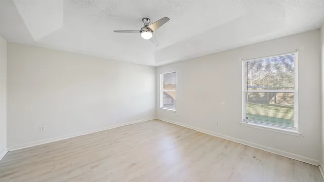 an empty room with wooden floor fan and windows