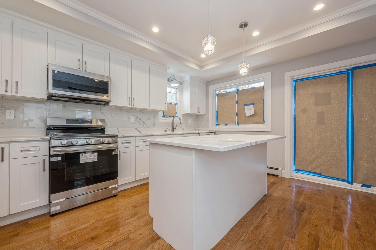 246-59 86th Road Queens, NY 11426 - Photo 13 of 44 Kitchen featuring white cabinetry, a center island, hanging light fixtures, a raised ceiling, and stainless steel appliances