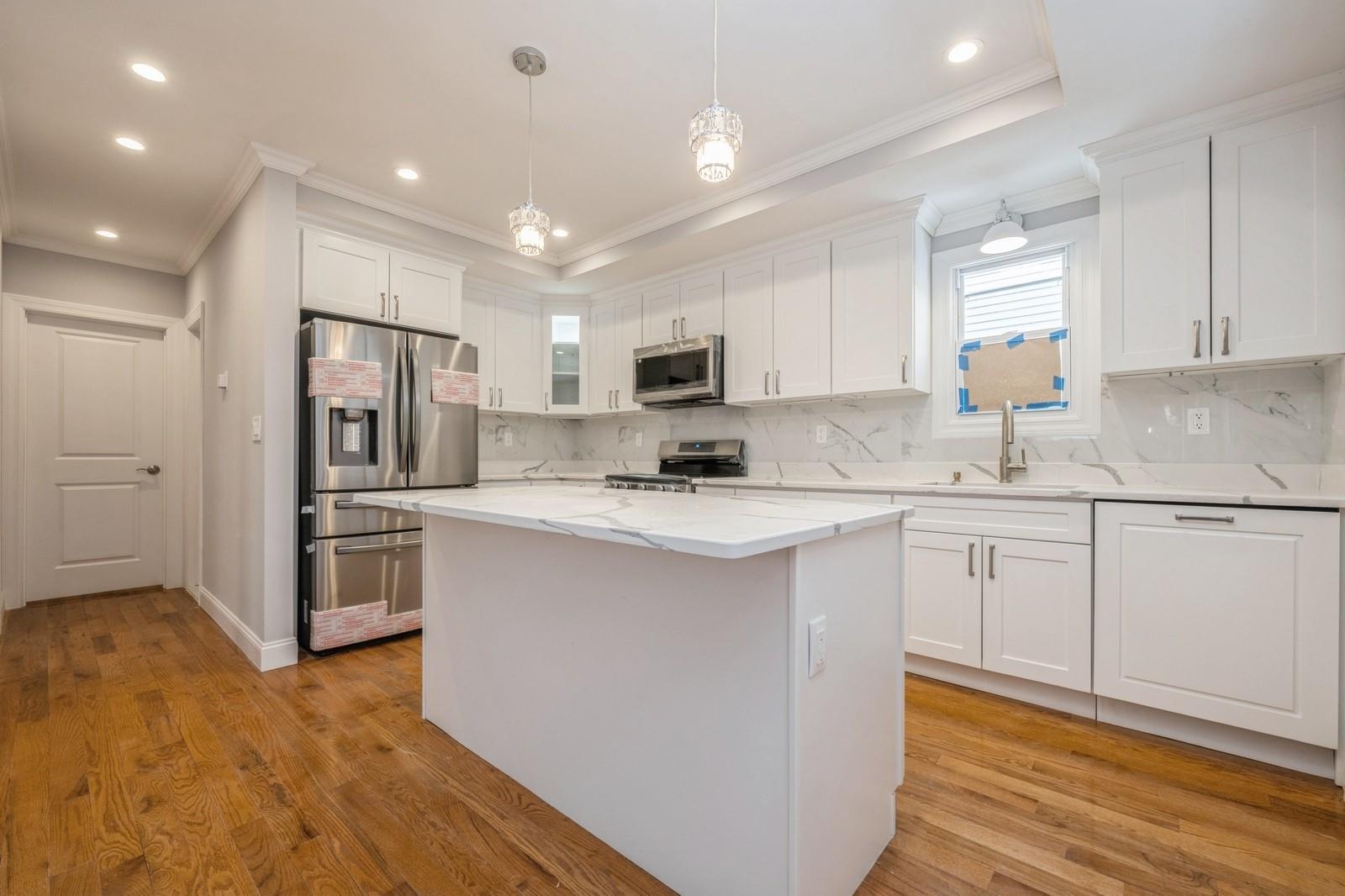 246-59 86th Road Queens, NY 11426 - Photo 15 of 44 Kitchen featuring sink, white cabinetry, hanging light fixtures, a kitchen island, and stainless steel appliances