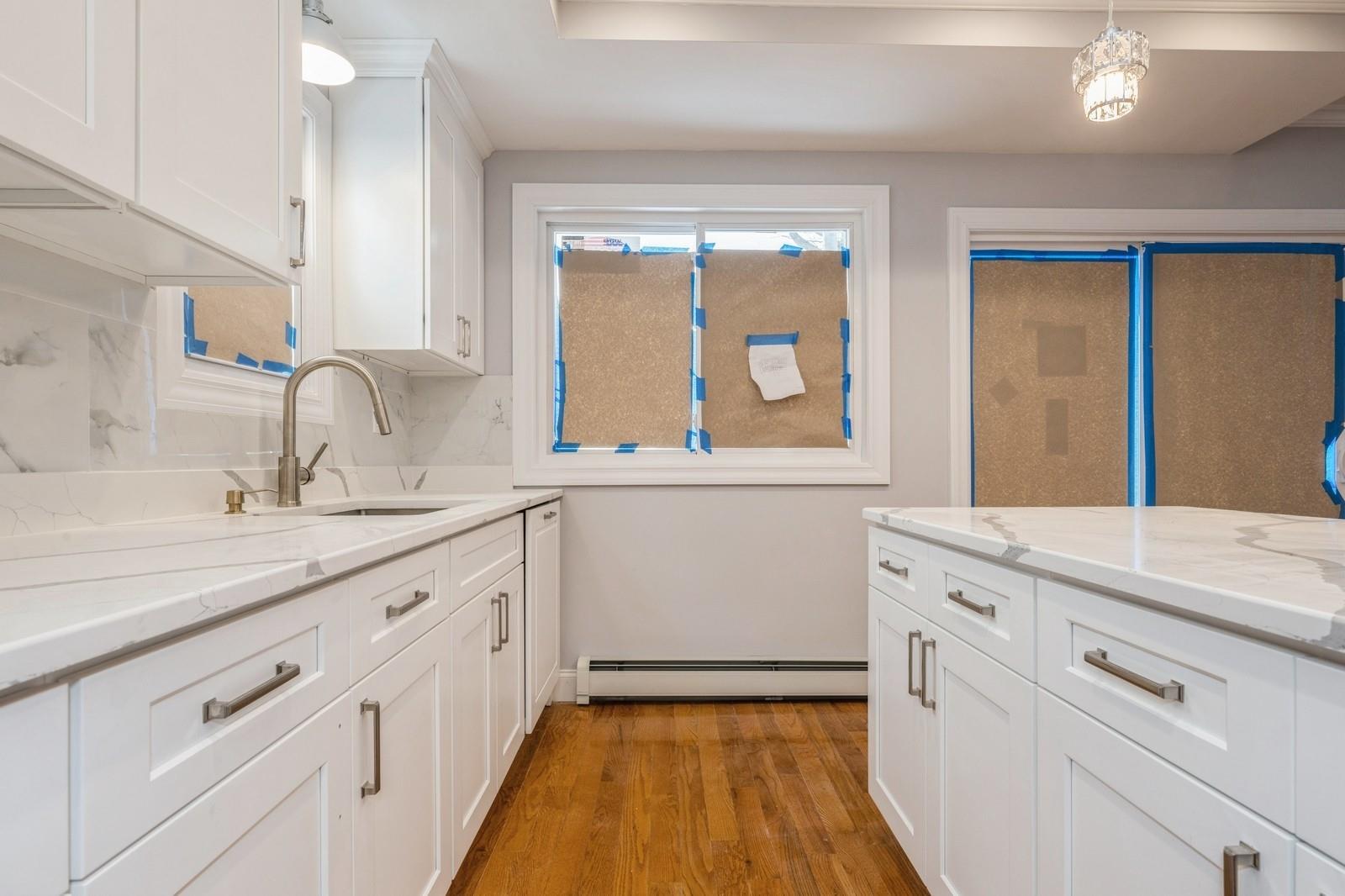 246-59 86th Road Queens, NY 11426 - Photo 16 of 44 Kitchen with decorative light fixtures, sink, white cabinets, light stone counters, and baseboard heating