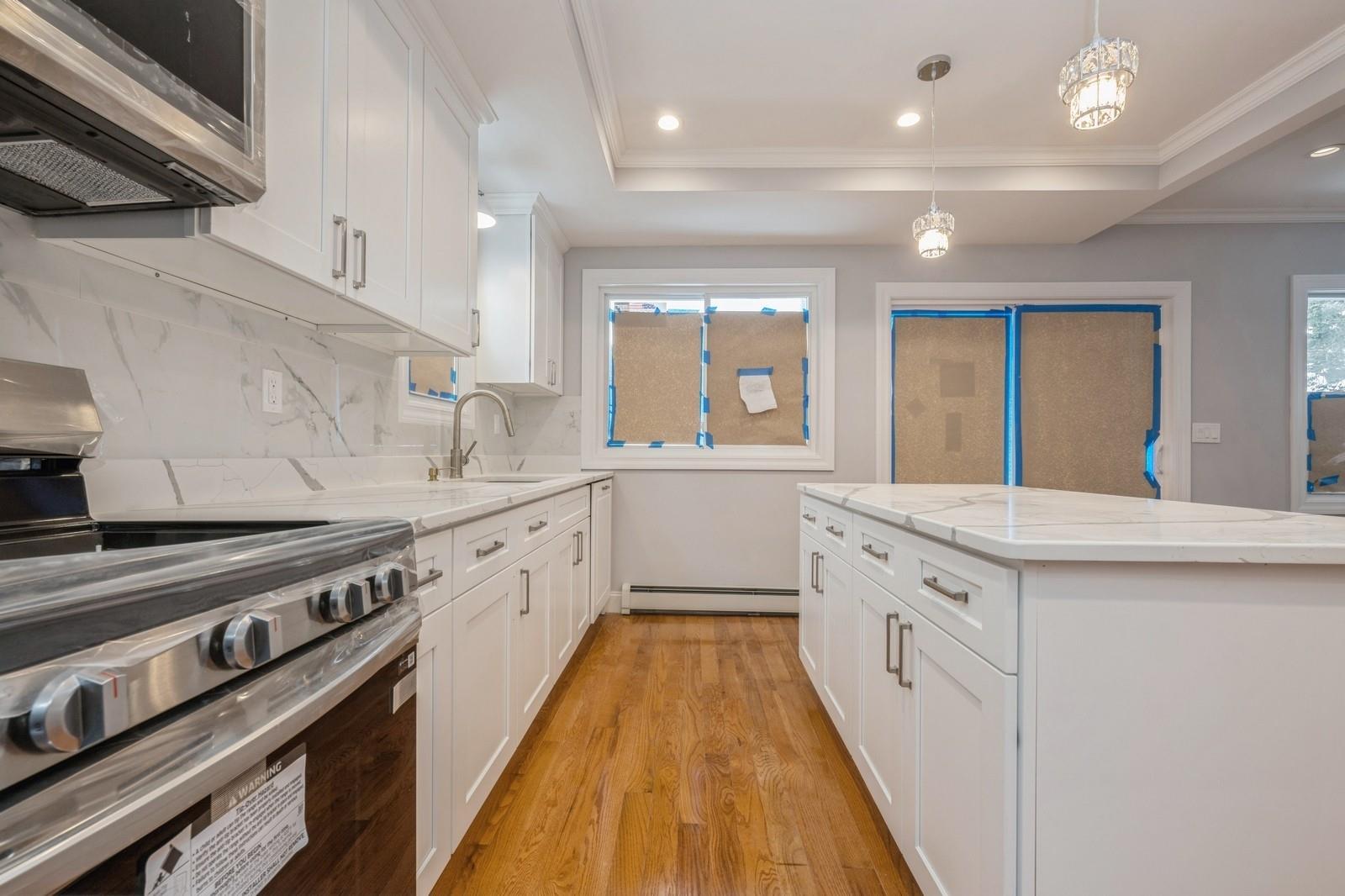 246-59 86th Road Queens, NY 11426 - Photo 17 of 44 Kitchen with a raised ceiling, a baseboard radiator, white cabinets, hanging light fixtures, and stainless steel appliances