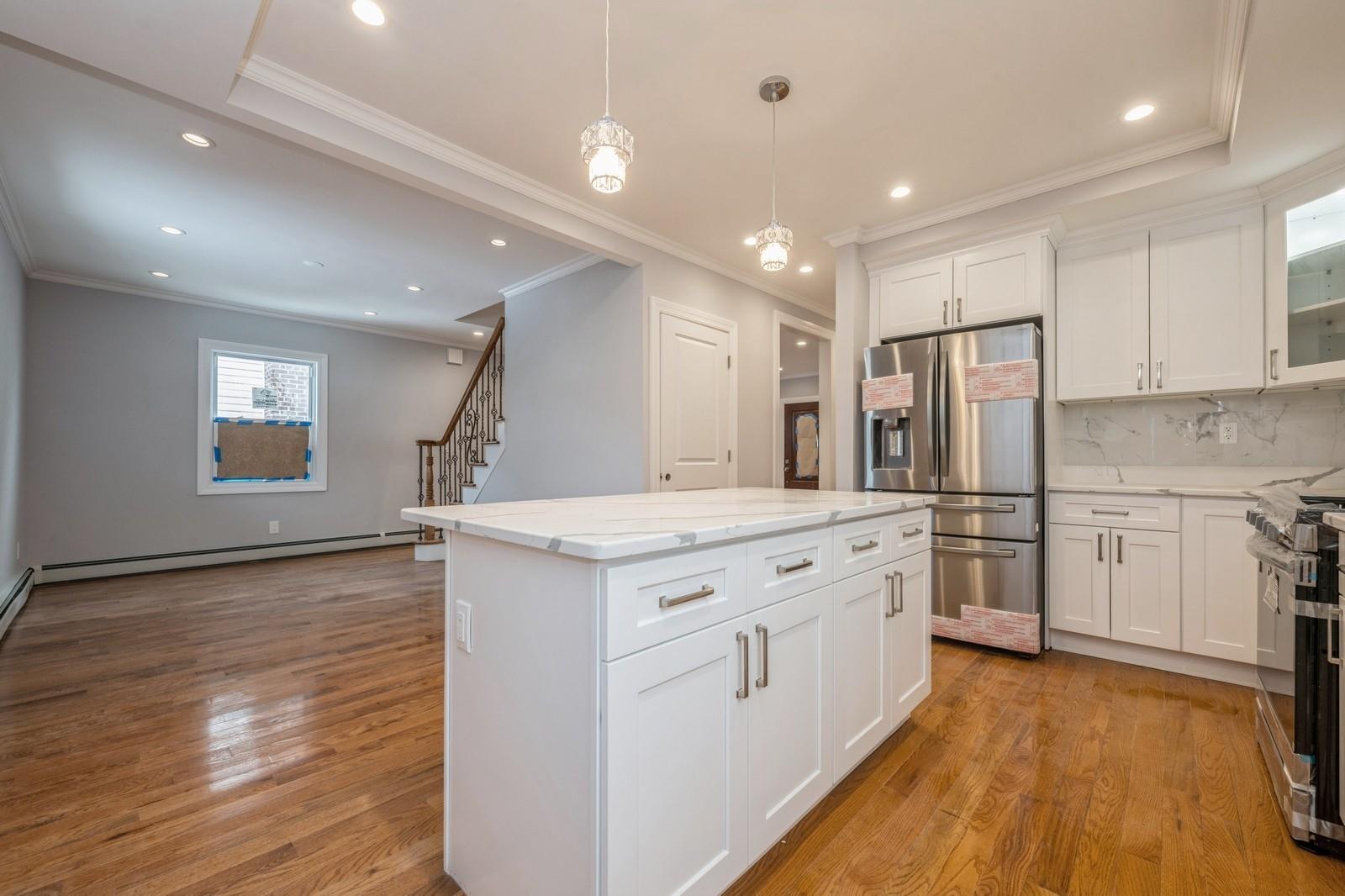 246-59 86th Road Queens, NY 11426 - Photo 19 of 44 Kitchen with white cabinetry, decorative light fixtures, a center island, stainless steel appliances, and a baseboard heating unit