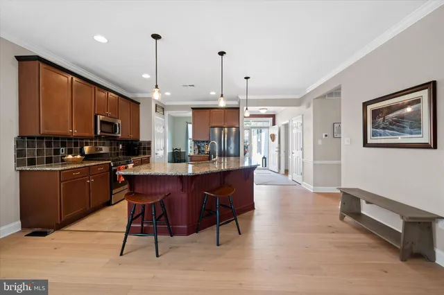 a kitchen with stainless steel appliances kitchen island granite countertop a refrigerator a stove a sink a dining table and chairs with wooden floor