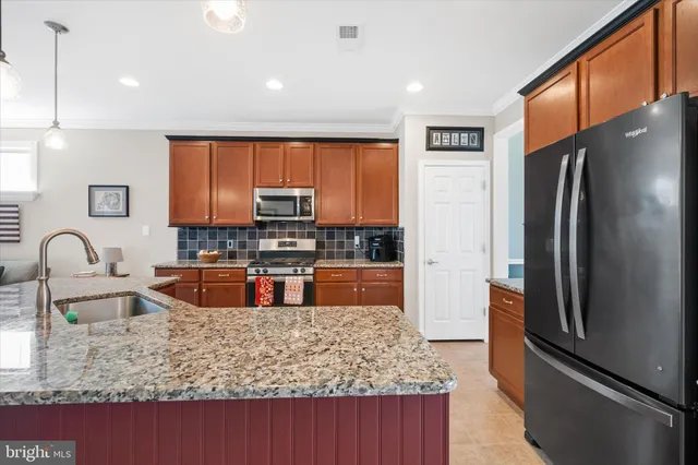 a kitchen with stainless steel appliances granite countertop a refrigerator a stove and a sink with wooden cabinets