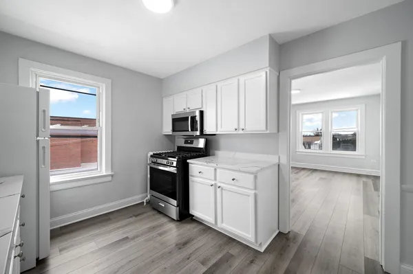 a kitchen with stainless steel appliances granite countertop a stove a sink and white cabinets with wooden floor