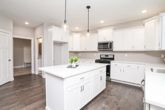 a kitchen with stainless steel appliances granite countertop a sink a stove a refrigerator and white cabinets with wooden floor