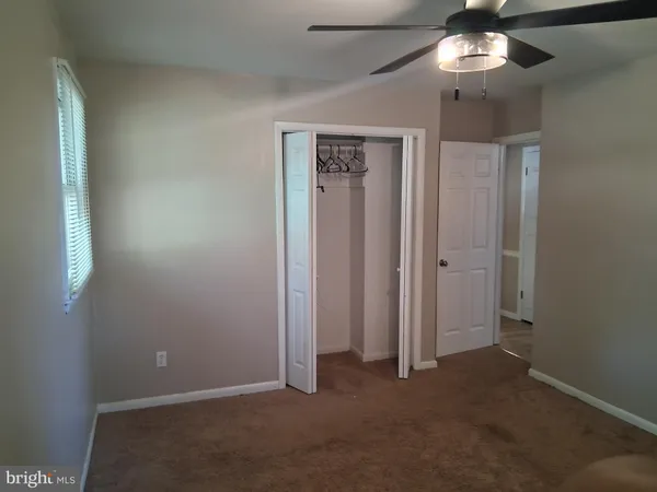 an empty room with a chandelier fan and closet area