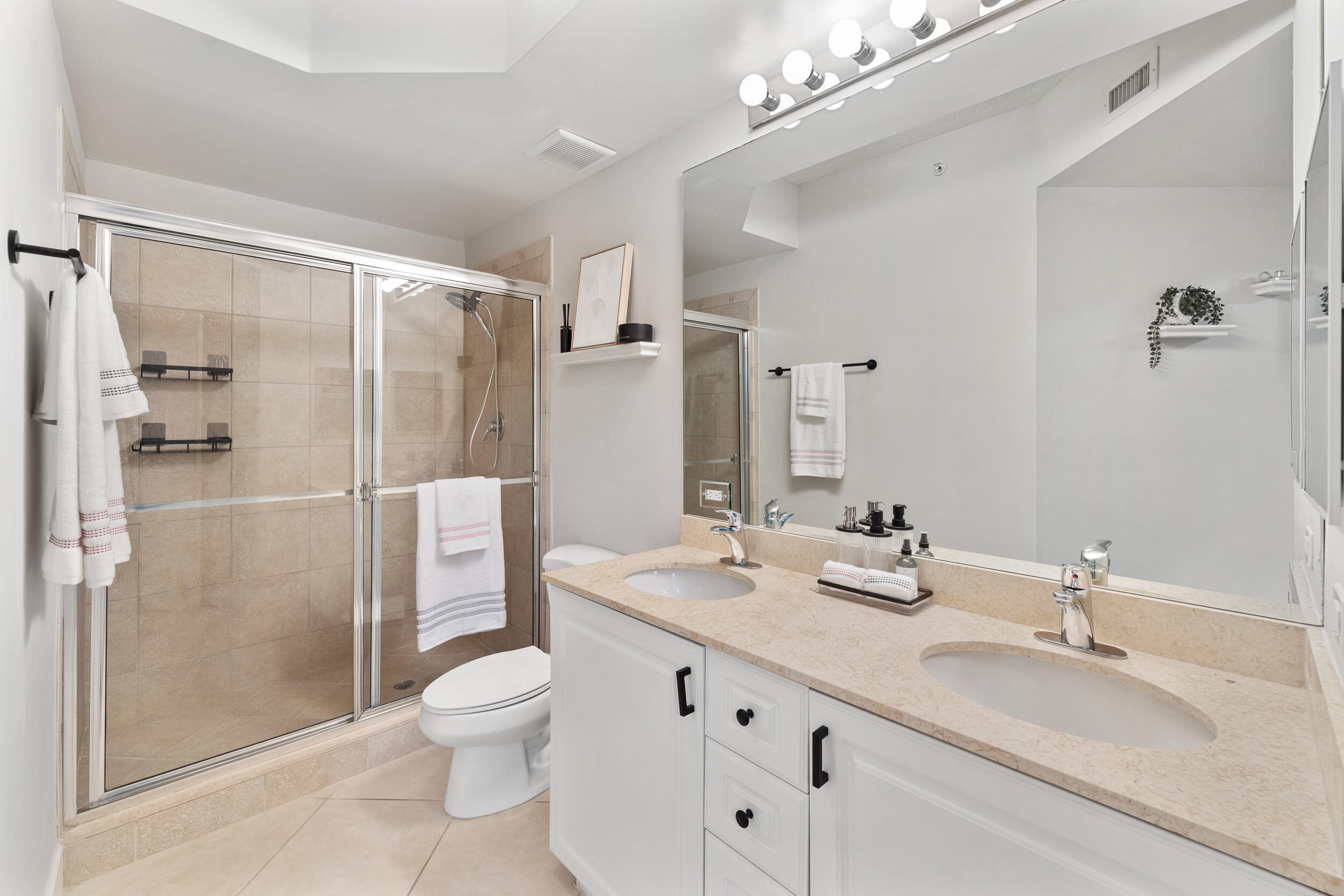 1690 Renaissance Commons Boulevard, Unit 1312 Boynton Beach, FL 33426 - Photo 11 of 39 a bathroom with a double vanity sink toilet mirror and shower