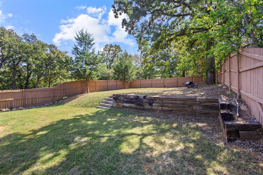 608 East Shepherd Street Denison, TX 75021 - Photo 28 of 31 Expansive backyard featuring a tiered landscape, privacy fencing, mature trees, wood retaining walls, and a grassy lawn