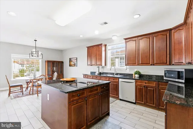 a kitchen with stainless steel appliances granite countertop wooden cabinets a sink dishwasher a stove and a refrigerator with wooden floor