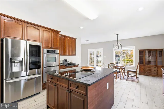 a kitchen with granite countertop a refrigerator a stove a sink a dining table and chairs with wooden floor