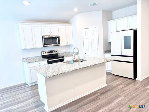 a kitchen with granite countertop a refrigerator a sink a stove a microwave and wooden floor