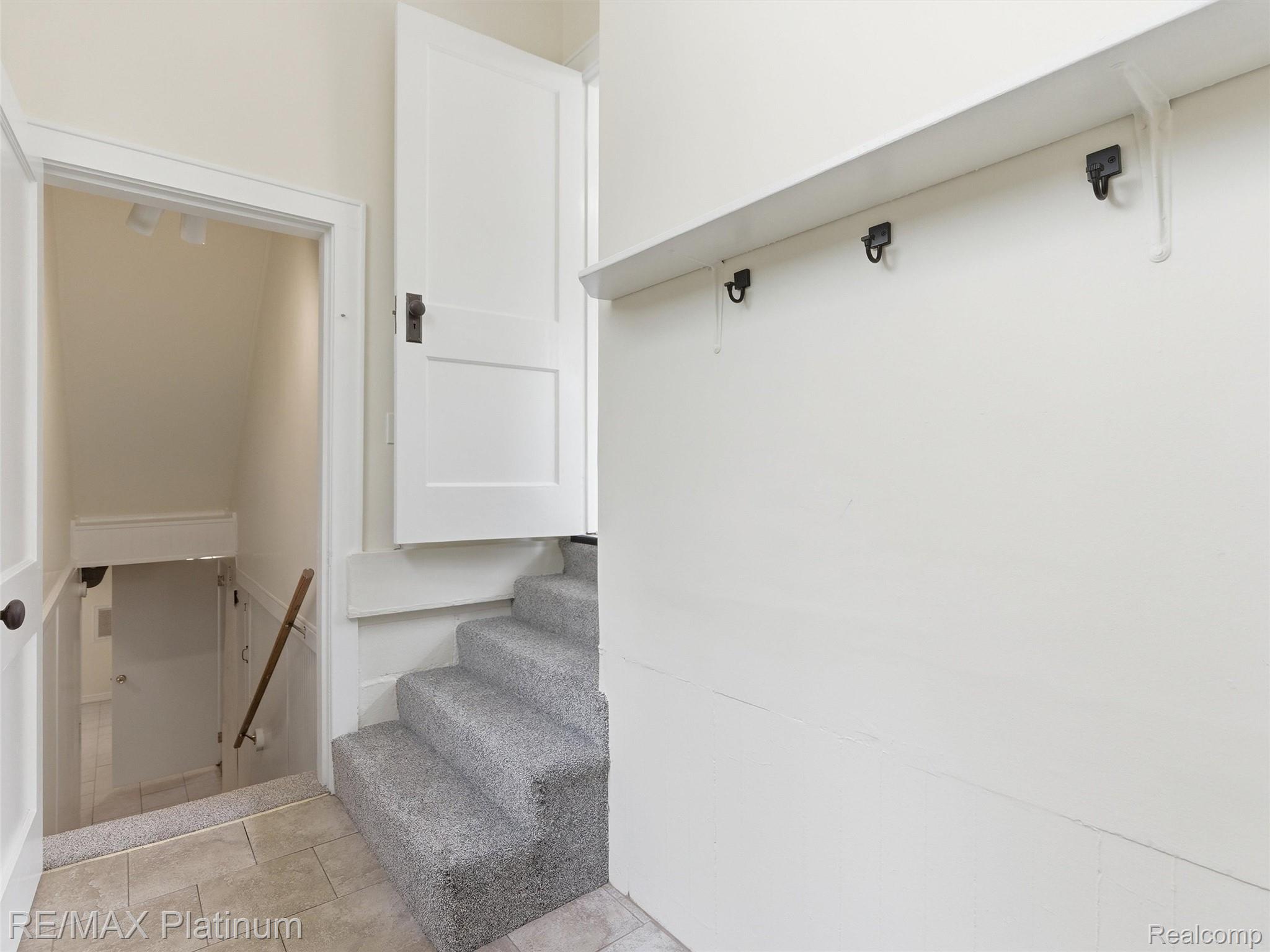 6335 Silver Lake Road Linden, MI 48451 - Photo 28 of 61 Carpeted staircase with an integrated shelf featuring hooks, alongside a doorway leading to a tiled floor landing with a wooden handrail