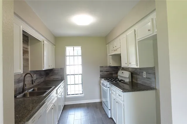 a kitchen with granite countertop a sink a stove and cabinets
