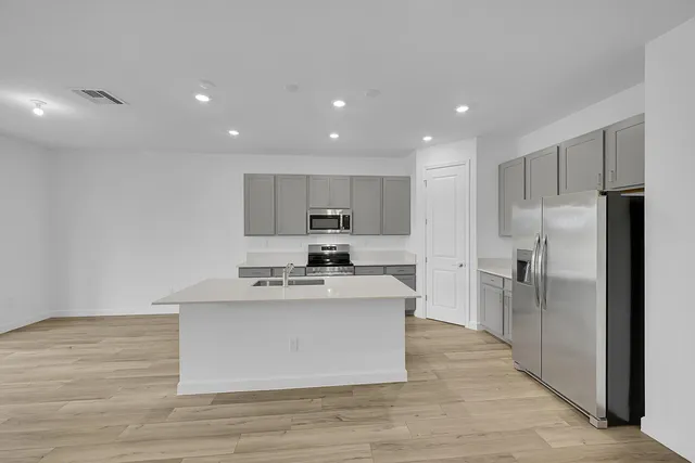 a large kitchen with stainless steel appliances a large counter top and a refrigerator