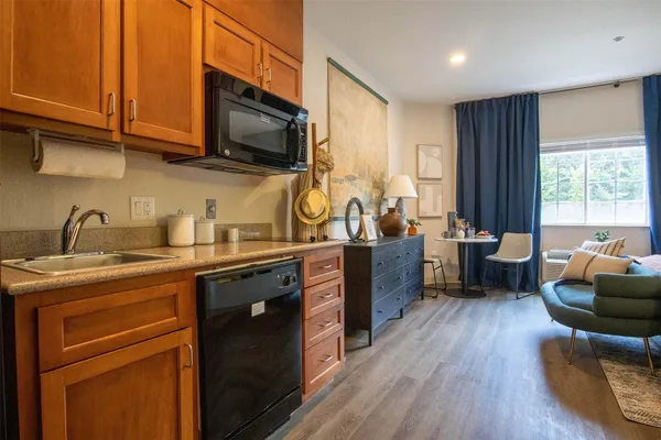 a kitchen with stainless steel appliances granite countertop a sink dishwasher stove and wooden cabinets with wooden floor