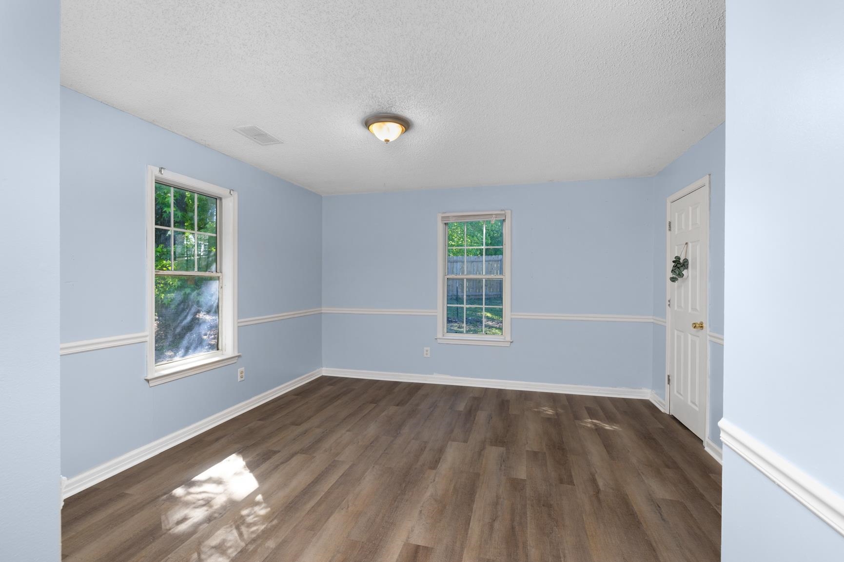 366 Adkins Road Burlison, TN 38015 - Photo 6 of 20 Spacious room featuring wood-finish flooring, light blue walls with white chair rail molding, two windows with natural light, and a white paneled door