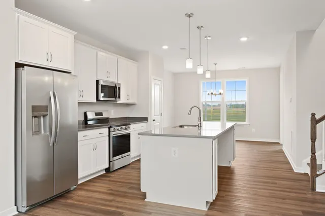 a kitchen with stainless steel appliances a sink a stove a refrigerator cabinets and a wooden floor