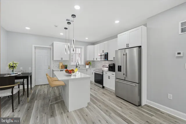 a kitchen view with stainless steel appliances a refrigerator a stove a dining table and chairs with wooden floor