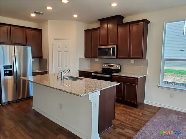 a kitchen with kitchen island granite countertop wooden cabinets a refrigerator and a sink