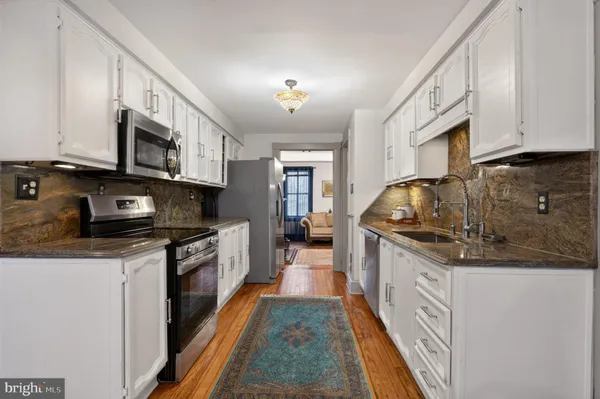 a kitchen with stainless steel appliances granite countertop a refrigerator a stove a sink dishwasher and white cabinets with wooden floor