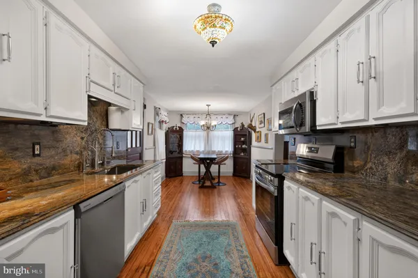 a kitchen with stainless steel appliances granite countertop a stove top oven a sink a dining table and chairs with wooden floor