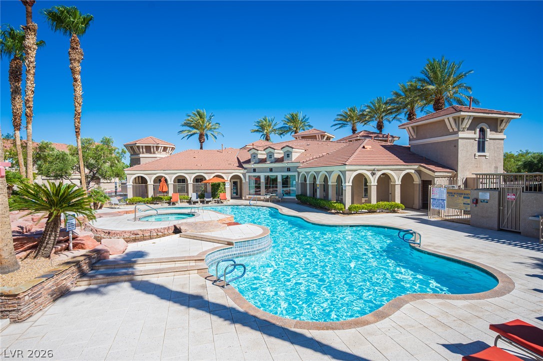 Palm trees frame a sparkling pool and spa adjacent to a Mediterranean-style clubhouse.