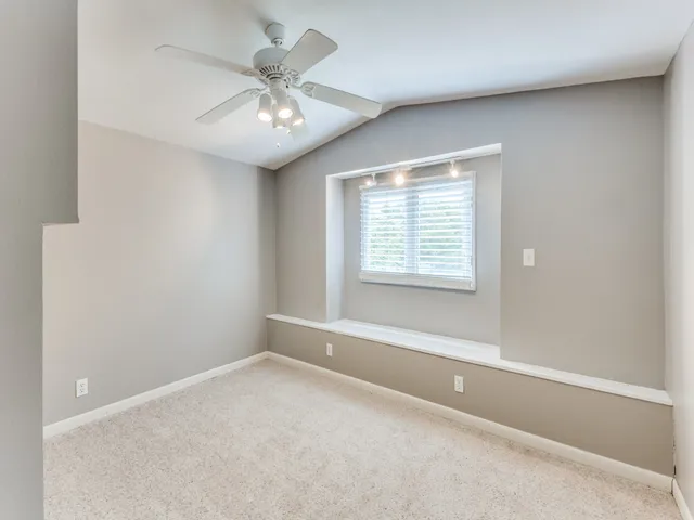 an empty room with a chandelier fan and windows