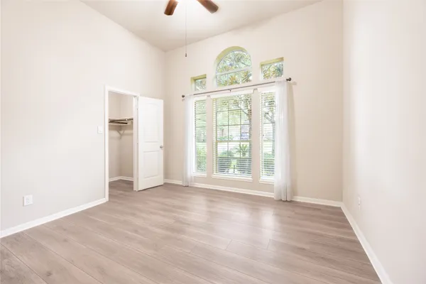 an empty room with wooden floor fan and windows