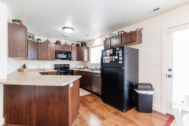 1145 West 2640th Street South Logan, UT 84321 - Photo 5 of 17 Kitchen featuring wood-finish flooring, a U-shaped peninsula with a light-toned countertop, dark wood cabinetry, and a black appliance suite including a refrigerator, range, and microwave