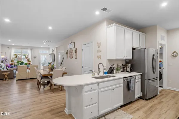a kitchen with a sink dishwasher a refrigerator and white cabinets with wooden floor