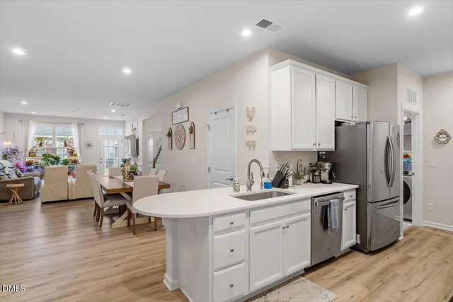 a kitchen with a sink dishwasher a refrigerator and white cabinets with wooden floor
