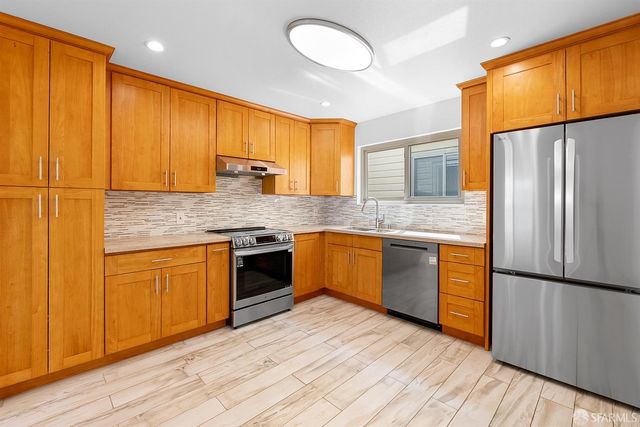 a kitchen with stainless steel appliances granite countertop a refrigerator a sink dishwasher a stove with wooden cabinets and floor