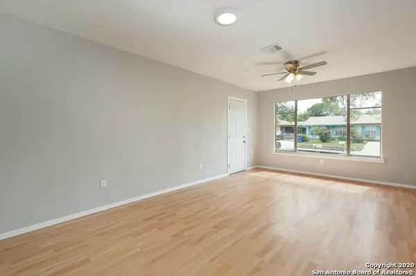 an empty room with wooden floor fan and windows