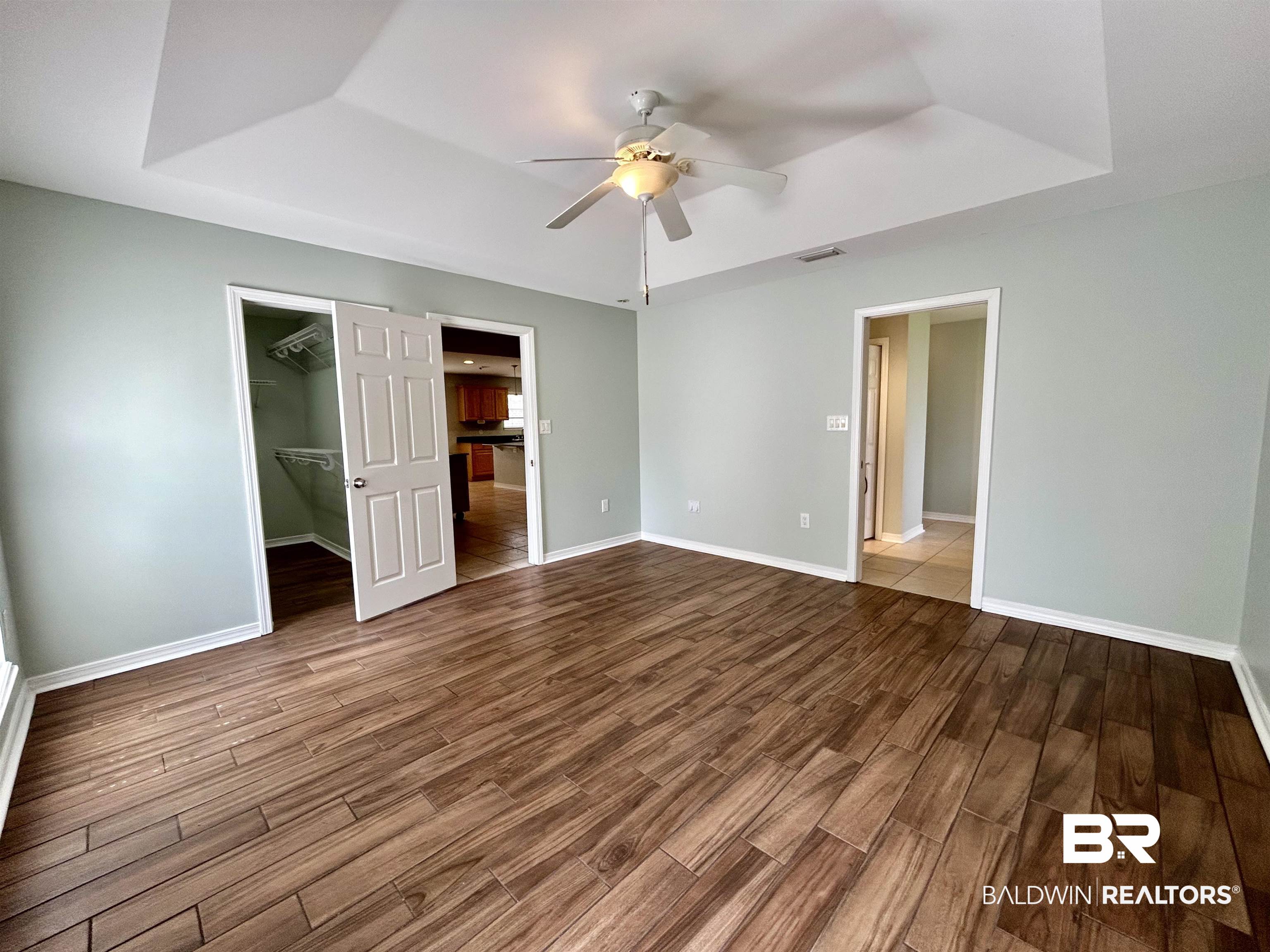 7198 Raintree Lane Gulf Shores, AL 36542 - Photo 13 of 33 Spacious room featuring wood-finish flooring, light green walls, a tray ceiling, and a ceiling fan
