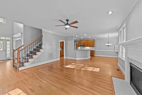 a view of an empty room and kitchen with wooden floor