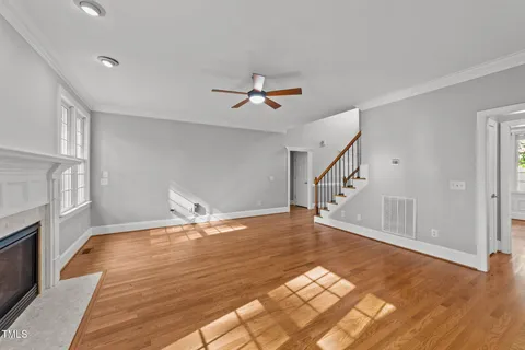a view of an empty room with chandelier fan and wooden floor