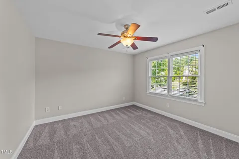 a view of an empty room with chandelier fan and window