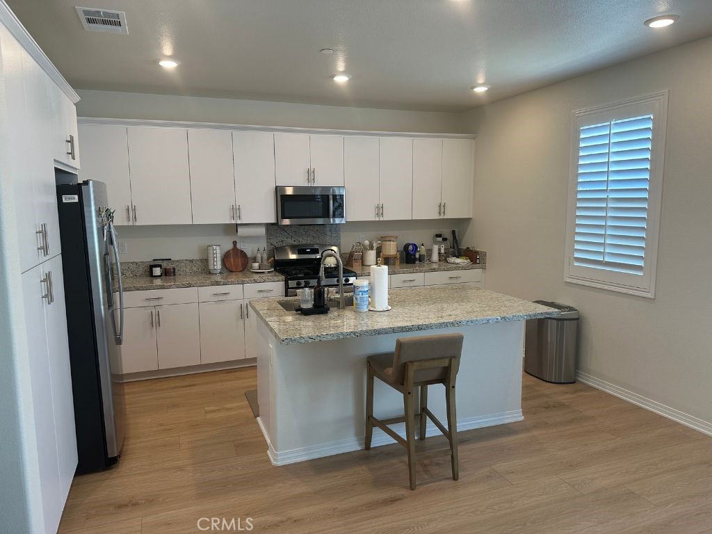 2511 Gunner Ridge Way Rialto, CA 92377 - Photo 14 of 37 a kitchen with stainless steel appliances granite countertop a table chairs sink refrigerator and cabinets
