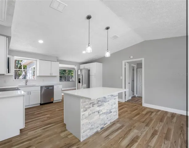 a large kitchen with kitchen island a stove a sink dishwasher a refrigerator and white cabinets with wooden floor